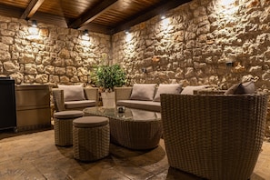 Une pièce aux murs de pierre, meublée d’un mobilier en osier, avec une table en verre et une plante en pot.