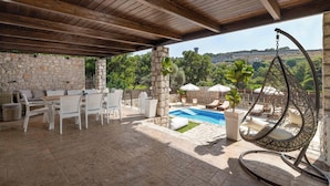 Un patio al aire libre con suelo de piedra, una piscina, muebles de mimbre y una silla colgante.