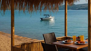 Una terraza de madera con una mesa preparada para dos, con vista al mar tranquilo y un barco a lo lejos.
