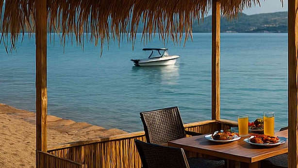 A wooden deck with a table set for two, overlooking a calm sea with a boat in the distance. - Antique İasos Butik Otel (Milas)