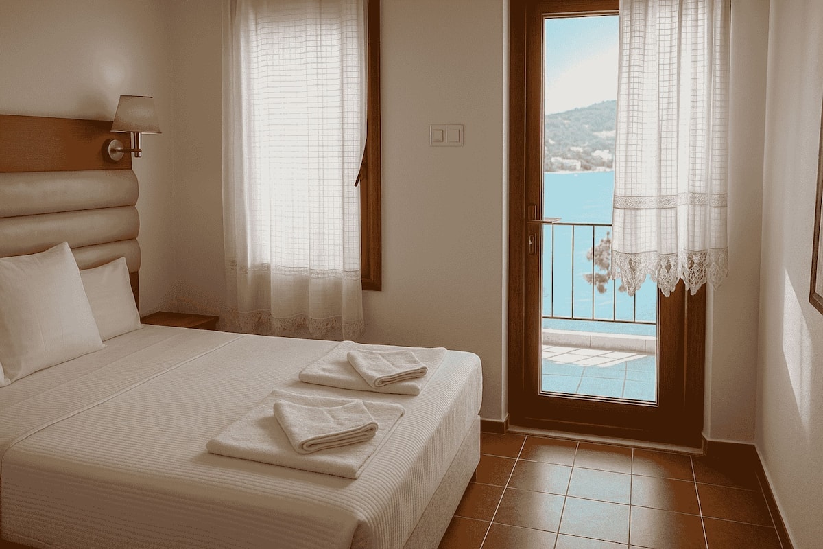 A bedroom with a bed, two windows with curtains, a view of the sea, and a balcony.