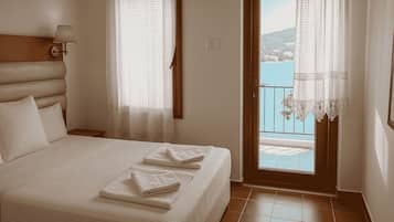 Un dormitorio con cama, dos ventanas con cortinas, vista al mar y un balcón.