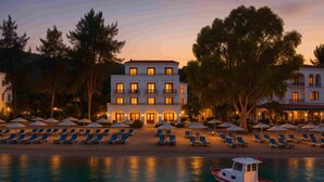 A waterfront hotel with multiple balconies, sun loungers, and umbrellas along the beach. - Antique İasos Butik Otel (Milas)