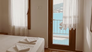 A bedroom with a bed, a window with curtains, and a view of a body of water and hills. - Antique İasos Butik Otel (Milas)