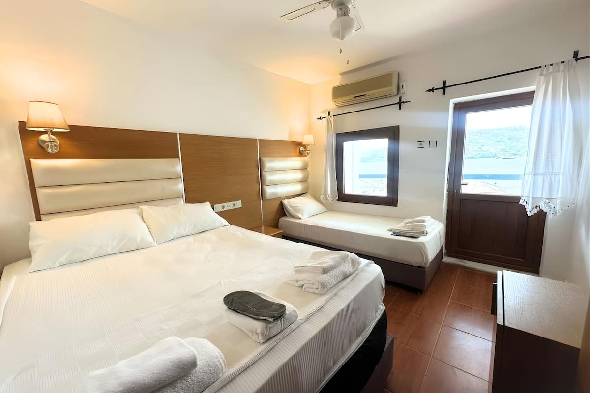 A hotel room with a large bed, a smaller bed, a window with a view, and a ceiling fan.