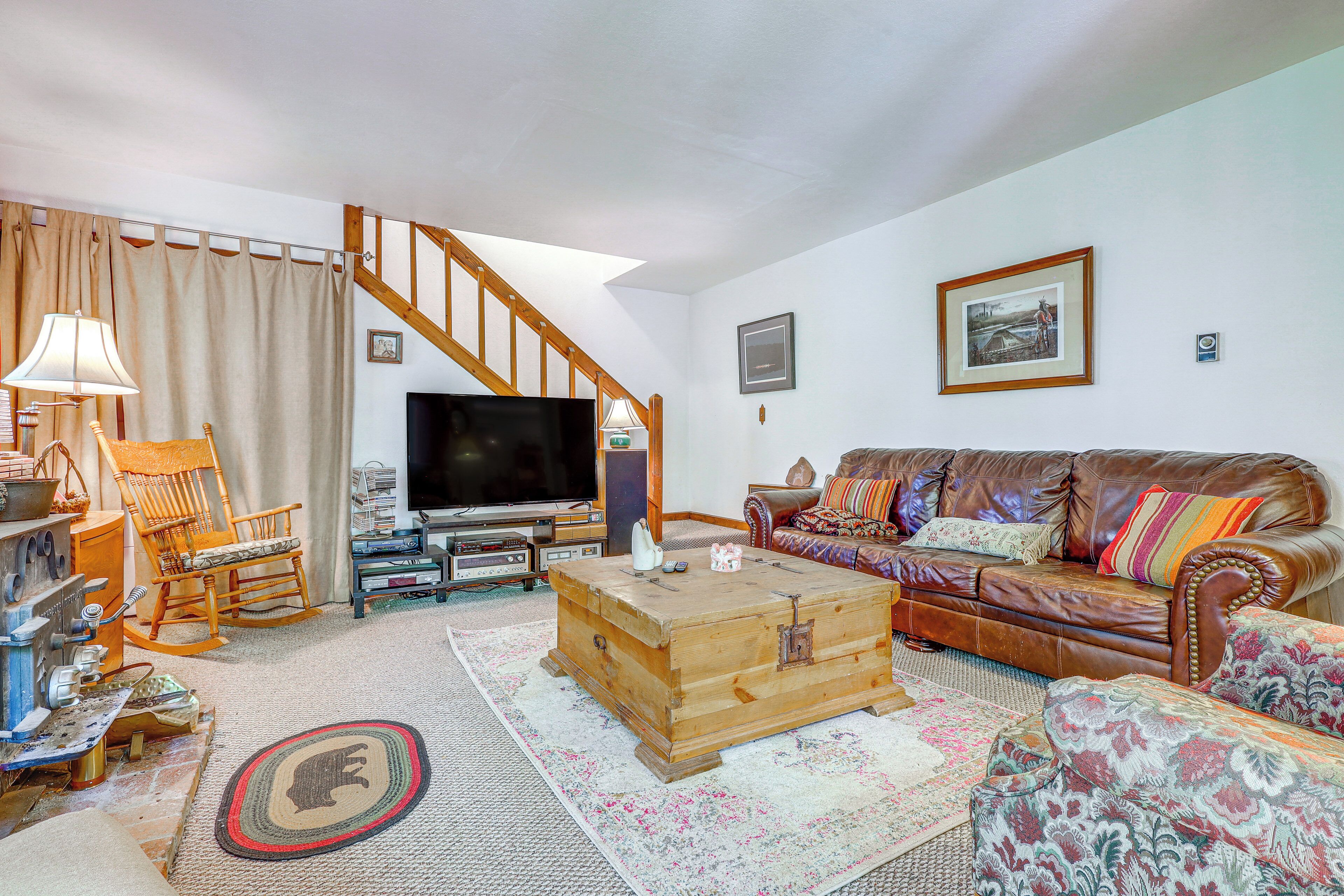 A living room with a wooden chest, a brown leather sofa, a wooden rocking chair, a television, and a staircase.