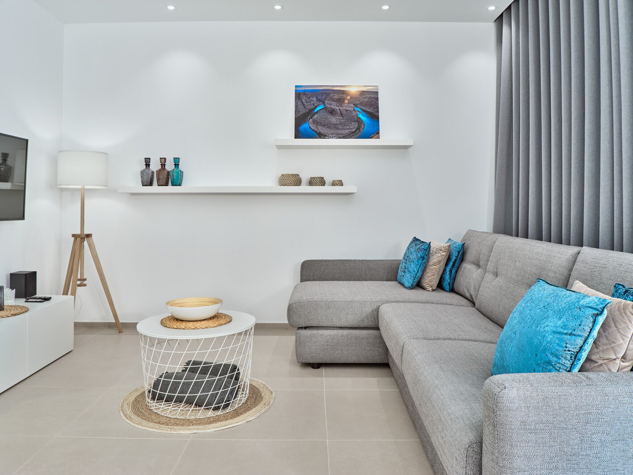 Uma sala de estar moderna com um sofá cinzento, uma mesa de centro redonda, um abajur e um quadro na parede.