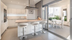 A modern kitchen with a central island, bar stools, and a view of the outdoor patio area. - Colinas - Tinerfe 1.1 NATURE RESERVE VIEW 2B (Arona)