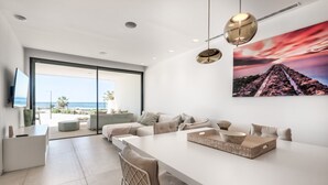 Un salon moderne avec une grande table à manger blanche, un canapé et une vue sur l’océan grâce à de grandes portes vitrées.