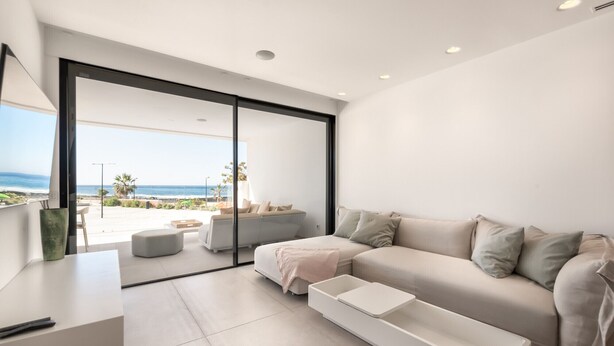 Un salon moderne avec un canapé, une table basse et une porte-fenêtre coulissante donnant sur un balcon avec vue sur l’océan.