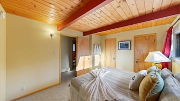 Ein Schlafzimmer mit Holzbalkendecke, einem Bett mit weißer Decke, Kissen und einem Nachttisch mit Lampe.