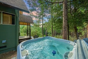 Ein Whirlpool in bewaldeter Landschaft mit einer Holzterrasse und einem Haus im Hintergrund.