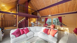 A spacious living area with a white sectional sofa, a dining table, and a kitchen in the background. - Rocky Raccoon | Hot Tub, Lily Rock Views & Fireplace (Idyllwild)