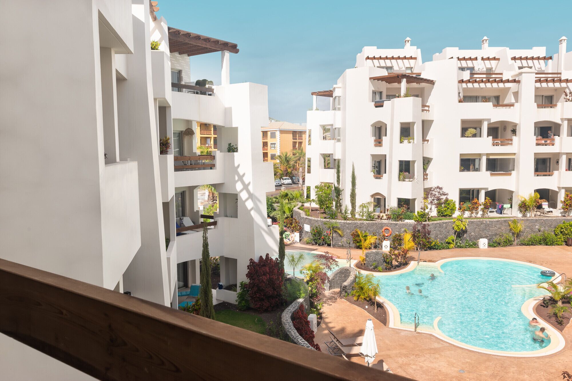 A modern hotel with a swimming pool surrounded by greenery and a clear blue sky.