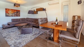 A modern living room with a sectional sofa, a dining table with chairs, a coffee table, and a rug. - Second Floor (Бјелиши)