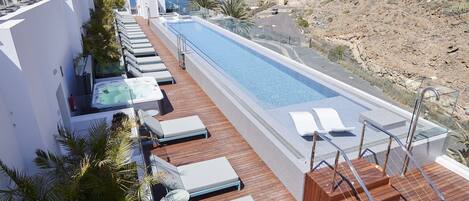 A rooftop pool area with lounge chairs, a hot tub, and a view of the sea.