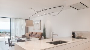 A modern kitchen with a large island, a dining area with a round table, and a sofa. - Infinity 1.2 LUXE PARTIAL SEA VIEW 2B (Arona)