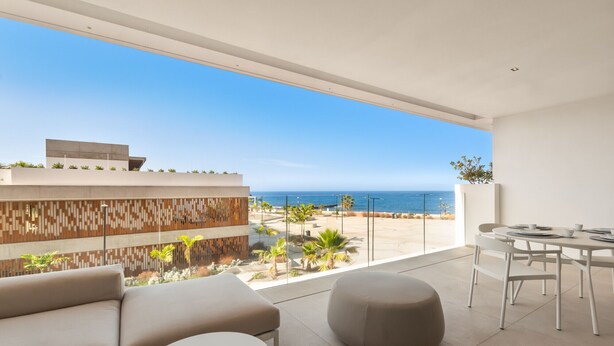 A modern living room with a large balcony, a sofa, a round table, and a view of the sea. - Infinity 1.2 LUXE PARTIAL SEA VIEW 2B (Arona)