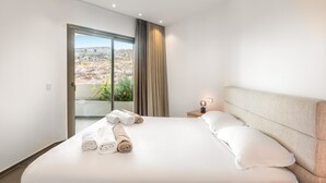 Een moderne hotelkamer met een groot bed, een nachtkastje met lamp en uitzicht op een woestijnlandschap door een schuifdeur.