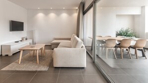 Een moderne woonkamer met een bank, salontafel en televisie. Er is een eethoek met stoelen en een tafel.