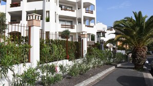 A multi-story residential building with balconies, a palm tree, and a street view.