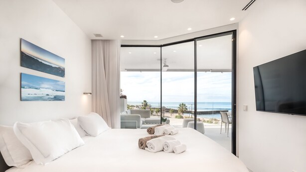Une chambre d’hôtel moderne dotée d’un grand lit, d’une télévision à écran plat et d’un balcon offrant une vue sur la mer.
