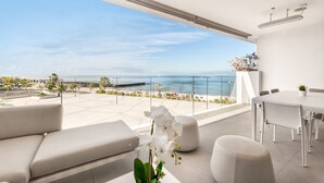 Un balcon moderne avec vue sur la mer, des meubles blancs et une plante en pot.