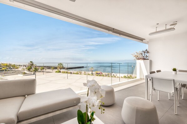 Un balcon moderne avec vue sur la mer, des meubles blancs et une plante en pot.