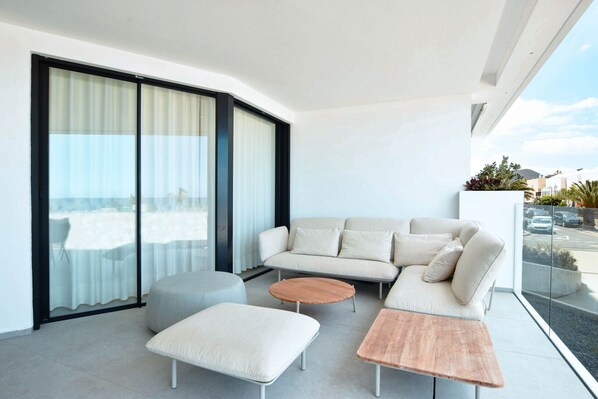 A modern outdoor living area with a sofa, ottoman, and round table, large sliding glass doors, and a view of the street.