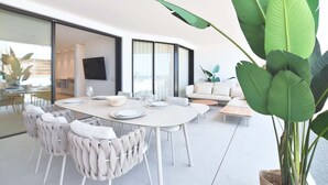 A modern dining area with a round table, white chairs, and a large potted plant. - Infinity 0.3 LUXE PARTIAL SEA VIEW 2B (Arona)