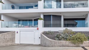 A modern multi-story residential building with a garage, a balcony, and a landscaped garden area. - Infinity 0.3 LUXE PARTIAL SEA VIEW 2B (Arona)