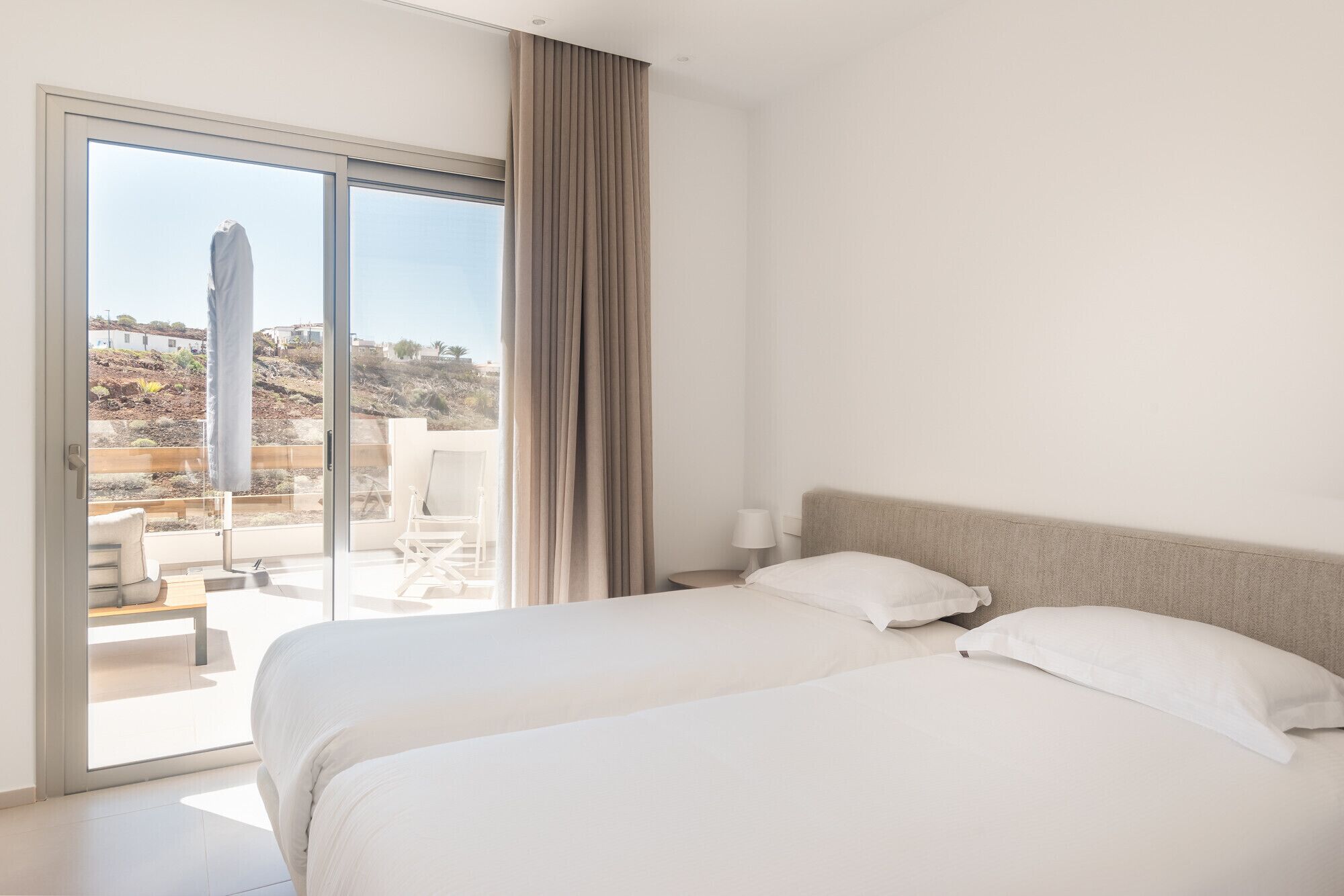 A hotel room with a large bed, a balcony with a chair, and a view of a hillside.