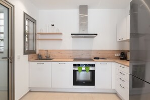 Une cuisine moderne avec des armoires blanches, une hotte de cuisinière en acier inoxydable, un four encastré et un réfrigérateur.