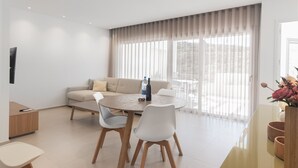 Un salon moderne avec un canapé, deux fauteuils, une table ronde et une grande fenêtre agrémentée de rideaux.
