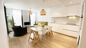 Une cuisine moderne avec des meubles blancs, une table à manger avec des chaises et des luminaires suspendus.