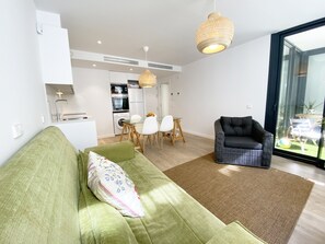 Ein modernes Wohnzimmer mit einem grünen Sofa, einem schwarzen Sessel und einem Essbereich mit weißen Stühlen.