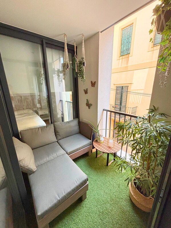 Ein Balkon mit einer grauen Couch, einem kleinen Tisch und Topfpflanzen.