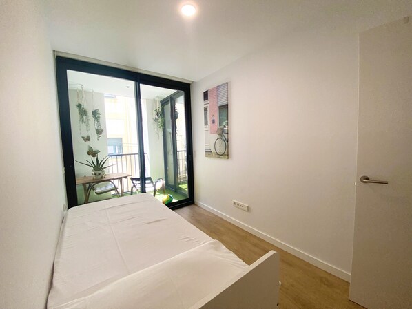 A bedroom with a bed, a sliding glass door leading to a balcony with a table and chairs, and a bicycle.