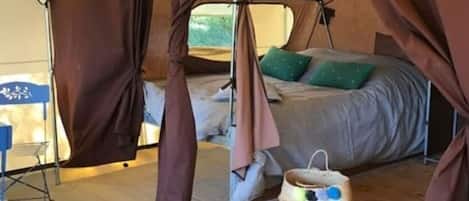 A tent with a bed, a small table, and a basket on the floor.
