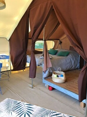 A tent with a bed, a small table, and a basket on the floor.