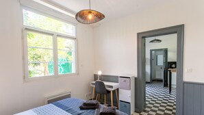 Une chambre à coucher avec un lit, un bureau et une chaise. Il y a une fenêtre qui donne sur un paysage verdoyant.