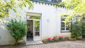Une cour pavée de pierres, avec un bâtiment blanc doté d’une porte et de fenêtres.