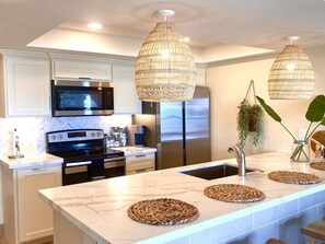 A modern kitchen with white cabinetry, stainless steel appliances, and a marble countertop.