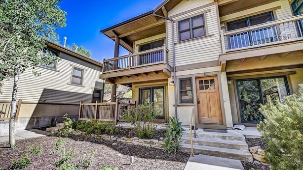 A multi-story building with a balcony on the second floor, a front door, and a small garden area with plants and steps leading to the entrance. - Greyhawk Condos - Corner Unit - Private Hot Tub (Park City)