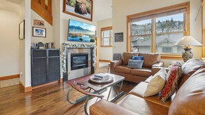 A cozy living room with a fireplace, a large window, and a comfortable seating area. - Greyhawk Condos - Corner Unit - Private Hot Tub (Park City)