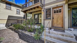 A two-story house with a wooden front door, a balcony, and a small garden area with plants and mulch. - Greyhawk Condos - Corner Unit - Private Hot Tub (Park City)