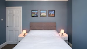 A bedroom with a bed, two bedside lamps, a door, and three framed pictures on the wall.