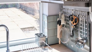 A kitchen with a clock, pots, pans, and utensils on shelves.