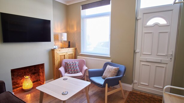A cozy living room with a flat-screen TV, a fireplace, a table, two chairs, and a window with a view.
