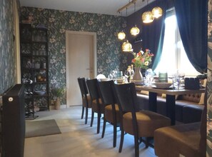Un coin repas avec une table dressée pour quatre personnes, entourée de chaises, avec une bibliothèque et une porte en arrière-plan.